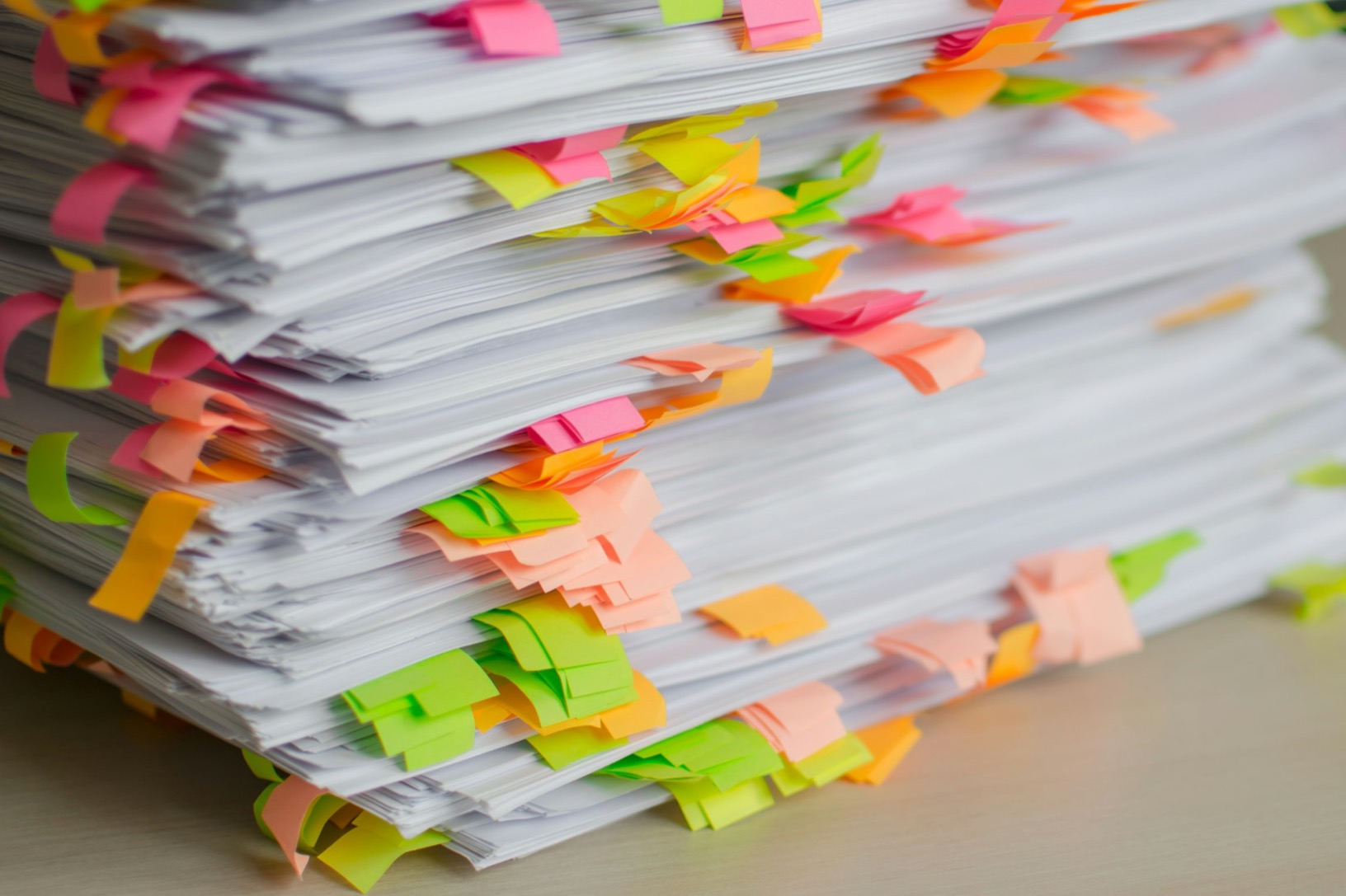 A tall stack of printed papers marked with coloured sticky tabs.