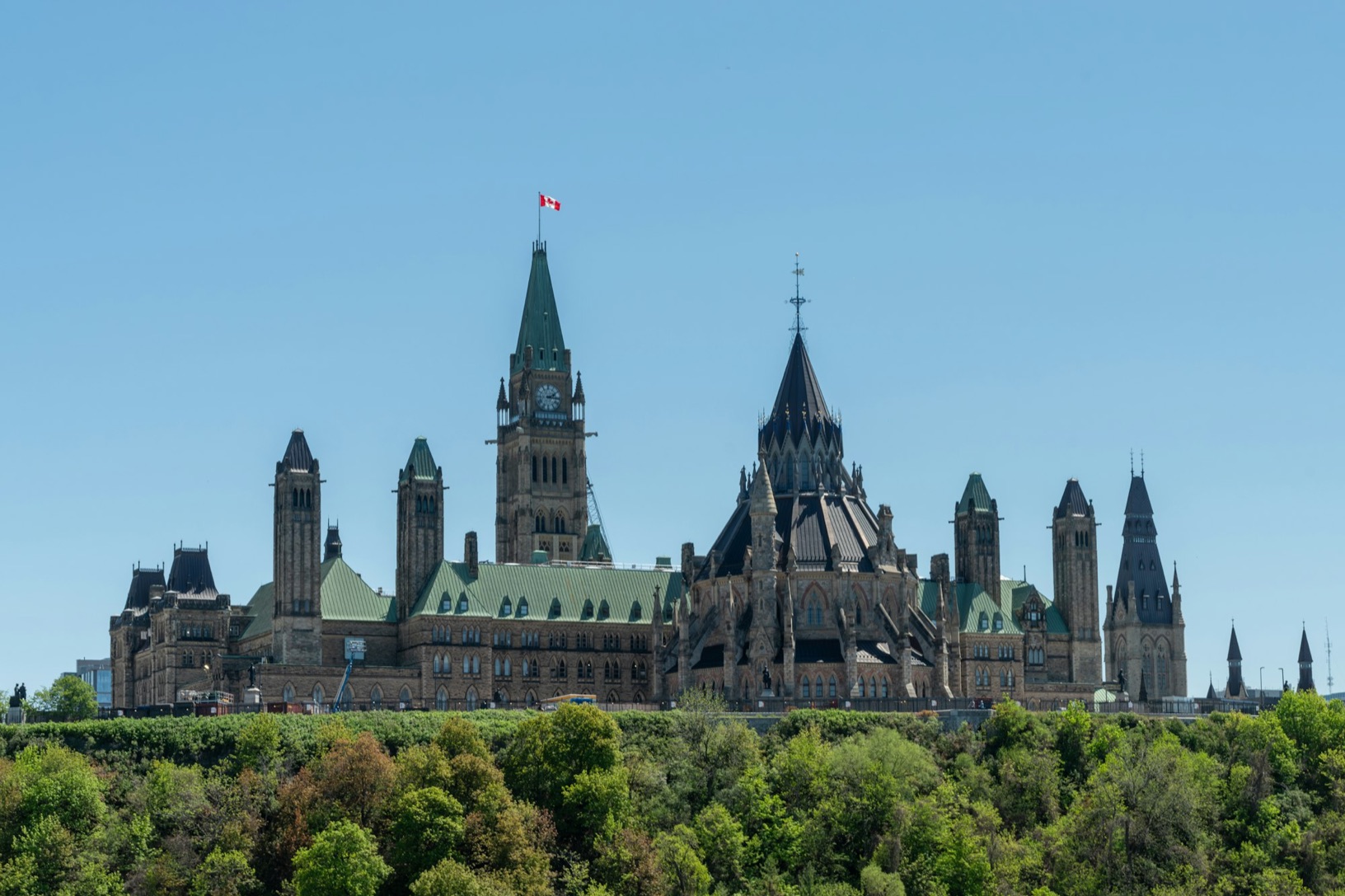 Parliament Hill in Ottawa above the trees, with the Peace Tower and the Library of Parliament under a clear sky.